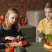 Positive little girl and boy sitting at desk with various fresh vegetables and fruits while preparing meal in loft kitchen with brick wall