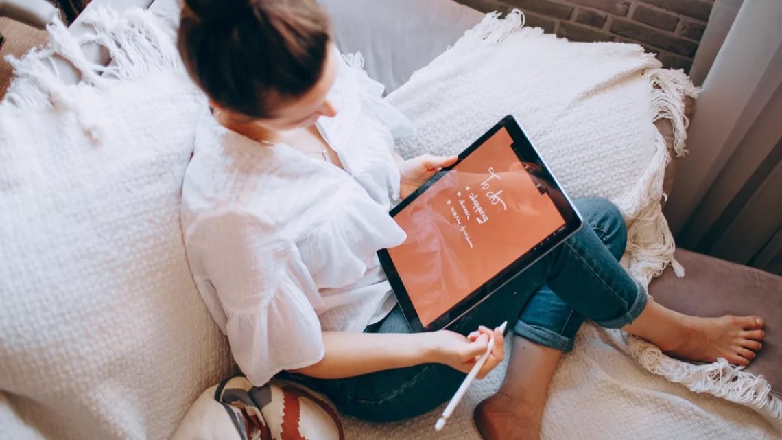 A woman relaxes on a sofa with a digital tablet, enjoying leisure time in a cozy home environment.
