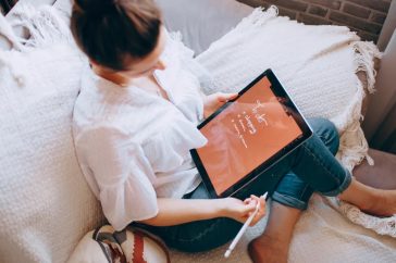 A woman relaxes on a sofa with a digital tablet, enjoying leisure time in a cozy home environment.