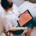A woman relaxes on a sofa with a digital tablet, enjoying leisure time in a cozy home environment.