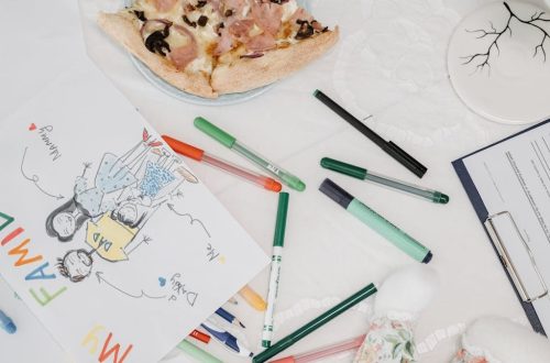 A colorful child's drawing of a family alongside pizza and pens on a table.